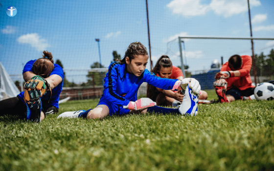 Young Athlete doing a hamstring stretch, wearing a blue football kit, sitting on the grass